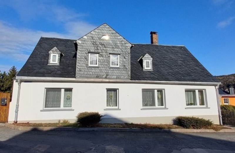 Dieses Bild zeigt ein weißes Einfamilienhaus in Schneeberg an einem hellen Tag unter blauem, bewölktem Himmel.