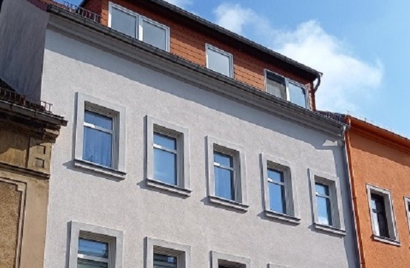 Dieses Bild zeigt ein weißes Etagenwohnhaus an einem hellen Tag unter blauem, bewölktem Himmel.