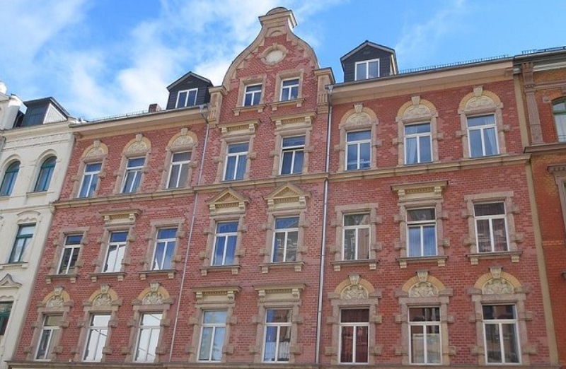 Dieses Bild zeigt ein rotes Etagenwohnhaus an einem hellen Tag unter blauem, bewölktem Himmel.