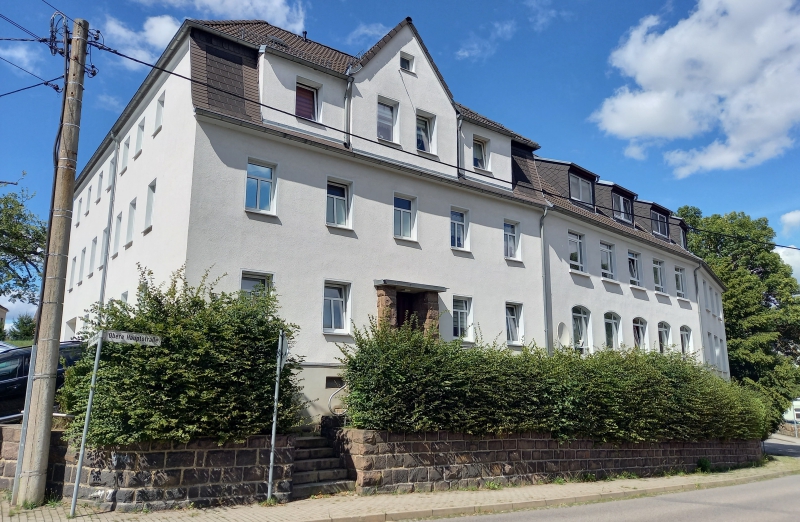 Dieses Bild zeigt ein weißes Etagenwohnhaus an einem hellen Tag unter blauem, bewölktem Himmel.