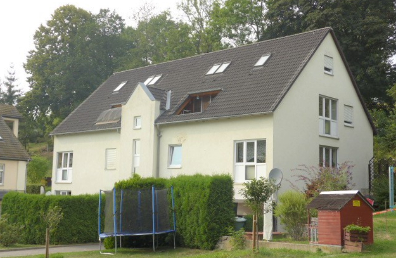 Dieses Bild zeigt ein weißes Etagenwohnhaus in Waldkirchen an einem hellen Tag unter blauem, bewölktem Himmel.