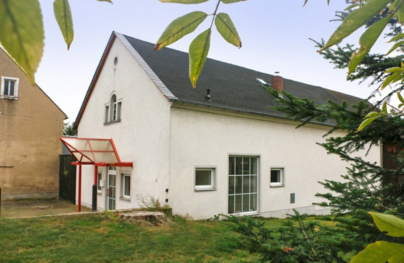 Dieses Bild zeigt ein weißes Haus in Röhrsdorf an einem hellen Tag unter blauem Himmel.