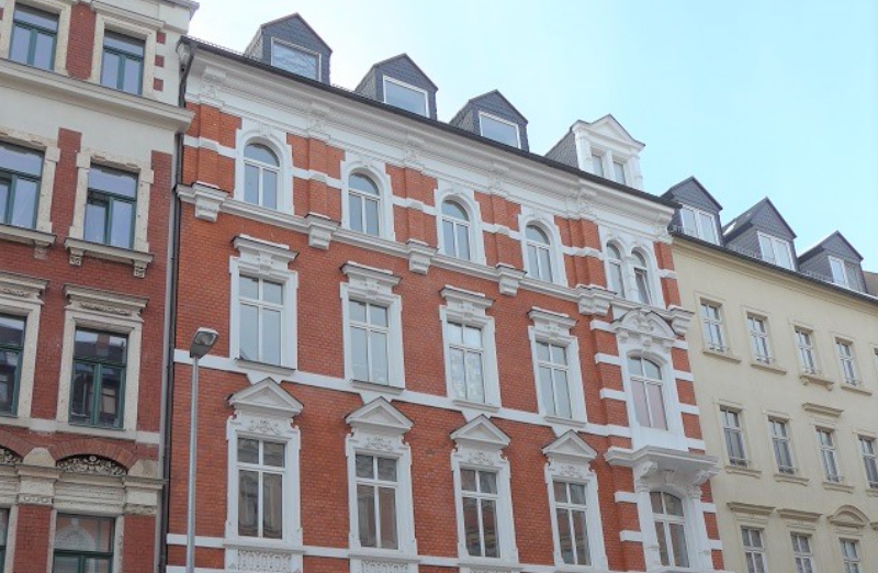 Dieses Bild zeigt ein rotes Mehrfamilienhaus in Chemnitz an einem hellen Tag unter klarem, blauem Himmel.