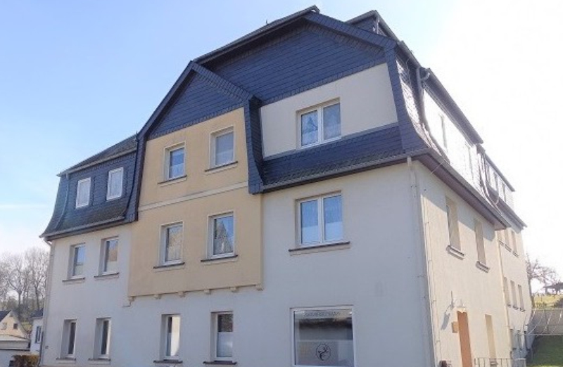 Dieses Bild zeigt ein oranges Mehrfamilienhaus in Drebach an einem hellen Tag unter klarem, blauem Himmel.