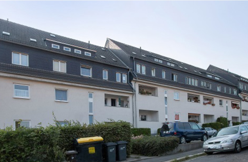 Dieses Bild zeigt ein weißes Reihenhaus mit Balkonen an einem hellen Tag unter blauem Himmel.